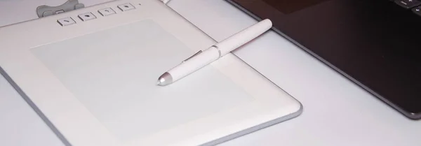 White graphics tablet on a white background. The work of a graphic designer. View of the top, side view. Tablet in macro. Pen stylus for drawing. Buttons on the tablet.
