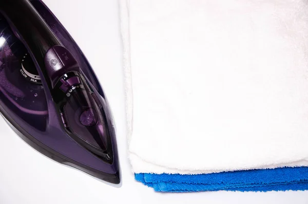 Modern iron on a white background with blue and white towels. View from the top, side. Macro. Iron and ironed things. Place for text