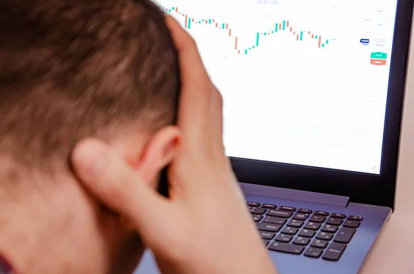 Trading on the exchange. A man is holding his head. Losing rates, promotions. Win, lose. Good luck and failure in trade. Focus on laptop and graphics