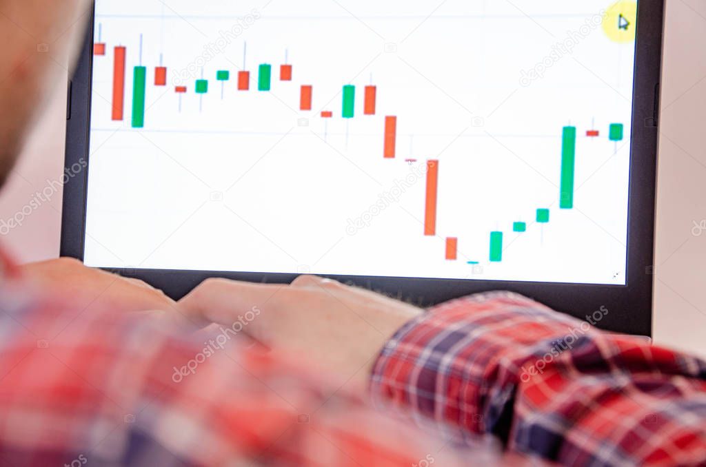 Trading on the exchange. Men's hands in a plaid shirt at a laptop. On-screen rates, promotions. Schedule. Wins are losses. Part of the back and head is visible. Focus on laptop and graphics