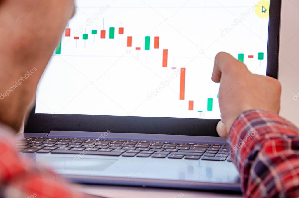 Trading on the exchange. Men's hands in a plaid shirt behind a laptop clenched into a fist. On-screen rates, promotions. Win, lose. Good luck and failure betting, trading. Focus on laptop and graphics