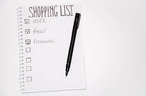 Shopping list. Squared notebook with black pen on a white background. Record ideas, notes, plans, tasks. The list includes bread, milk, bananas. Copy Spase