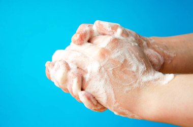 Kadınların elleri sabun tutuyor. Ellerinde sabun köpüğü var. Ellerinde sarı sabun var. Kadın sabunu mavi arka planda elleri yan gören bir şekilde yıkıyor. Virüs koruması. COVID-19
