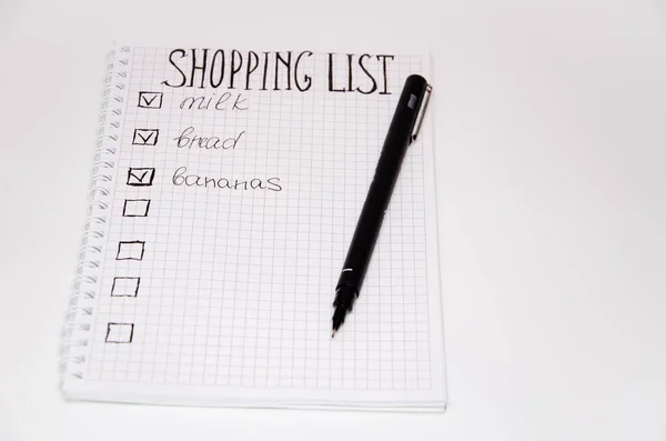 Shopping list. Squared notebook with black pen on a white background. Record ideas, notes, plans, tasks. The list includes bread, milk, bananas. Copy Spase