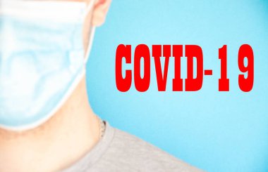 Mavi tıbbi maskeli bir adam kameraya yan yan bakıyor. Mavi arka planda gri tişörtlü bir adam. Mesaj için yer. Uzayı kopyala Covid 19