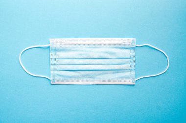 Mavi bir tıbbi maske mavi arka planda tek başına yatar. Mesaj için yer. Uzayı kopyala COVID-19