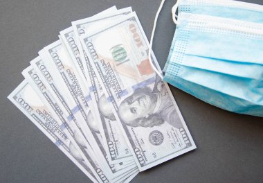 Mavi, sarı, pembe arka planda dolarları olan mavi tıbbi maske. Siyah arka planda maske ve 100 dolarlık banknotlar. Uzayı kopyala COVID-19