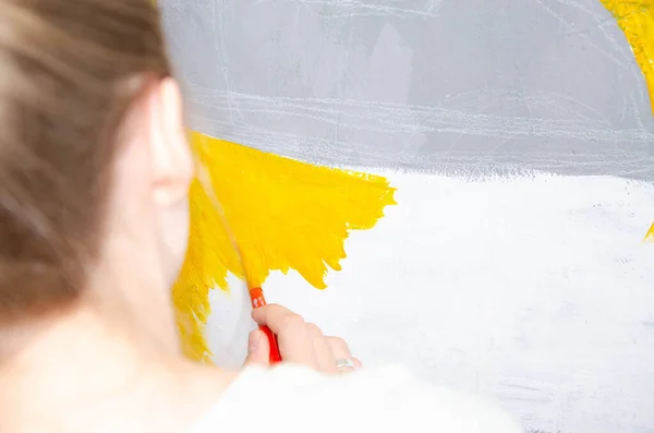 stock image Young girl designer draws a city drawing with paints on a gray wall