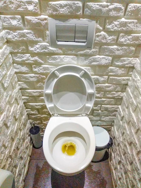 Dressing room with a white toilet. The room is made of white decorative stone, tiles. Urine in the toilet. Male hand flushes the toilet, first-person view