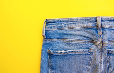 Sarı arka planda kot pantolon. Kot pantolon, cepler, yakın plan dikişler. Yırtık kot pantolon. Boşluğu Kopyala