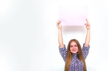 Ekose gömlekli, uzun saçlı genç bir kız geniş bir çarşaf tutuyor. Önünde bir çerçeve var. Kendinden yukarıda, yandan. Kız gösterir, sunar, puan verir.