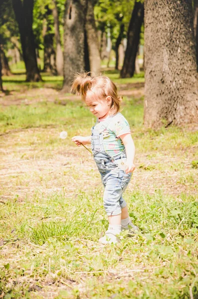 May 2020 基辅乌克兰 一个小女孩在外面的一个公园里玩耍 在一个阳光灿烂的日子里 穿着斜纹棉布工作服和印有Lol图案的T恤衫收集植物 — 图库照片