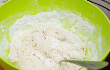 Bir kadın eli maya, su ve şeker dolu bir kaseye un döker. Pizza hamuru yapmak