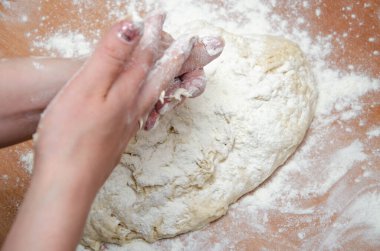 Kadın elleri yoğurur, pizza hamurunu yoğur. Hamur, un, aşçı, pizza. Kız merdane hamuru