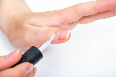 Evde manikür, karantina sırasında. Ev manikürü. Kız şeffaf cila sürmüş, tırnak yağı sürmüş, tırnakları beyaz arka planda, tırnağı da tırnak fırçasıyla. Makro