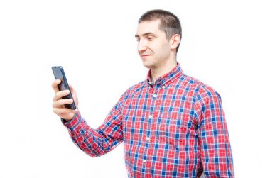 Beyaz arka planda akıllı telefonu olan ekose gömlekli genç bir adam. Adam akıllı telefona baktı ve telefonu onun önünde tuttu.