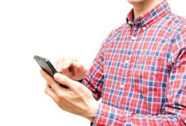 Beyaz arka planda akıllı telefonu olan ekose gömlekli genç bir adam. Adam kameraya bakar ve önünde bir akıllı telefon tutar ve parmağıyla işaret eder.