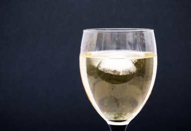 Parçalı bir bardak beyaz şarap, buz küpleri. Siyah arka planda buzlu şarap. Siyah bacaklı cam.