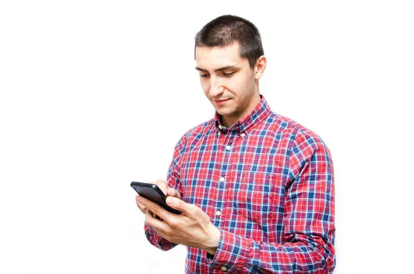 Beyaz arka planda akıllı telefonu olan ekose gömlekli genç bir adam. Adam akıllı telefona baktı ve telefonu onun önünde tuttu.