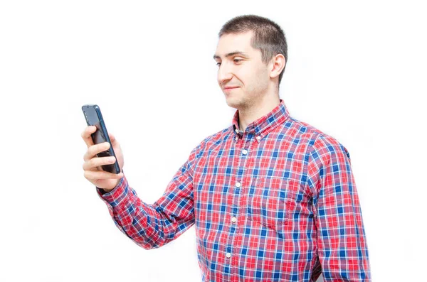 Beyaz arka planda akıllı telefonu olan ekose gömlekli genç bir adam. Adam akıllı telefona baktı ve telefonu onun önünde tuttu.