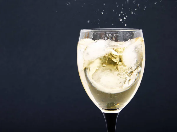 一杯白葡萄酒配上冰块冰块黑色背景上加冰块的葡萄酒 黑腿的杯子 从一杯加冰的葡萄酒中喷出 — 图库照片