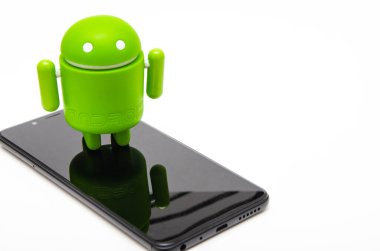 Android biblo ve akıllı telefon. Ekolojik plastikten yapılmış yeşil android heykeli siyah bir akıllı telefonun üzerinde duruyor.