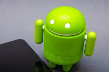 Android biblo ve akıllı telefon. Siyah arka planda ekolojik plastikten yapılmış yeşil Android heykelciği. Akıllı telefon onun hemen yanında duruyor..