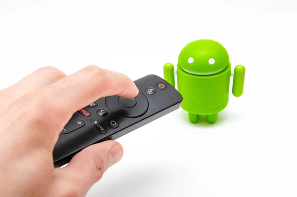 Android figür ve uzaktan kumanda. Beyaz arka planda yeşil plastik figür, akıllı televizyonun uzaktan kumandasının yanında, set üstü kutular. Erkek el kumandayı tutar ve androidi işaret eden düğmeye basar