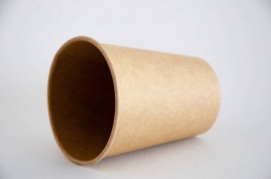 Kahve, çay için kahverengi kağıt bardak, beyaz arka planda çevresel malzemelerden bir içecek. Kâğıt bardaklardan biri yan yatar ve bir gölge düşer. Gri arka planda boynu yana yatık bir cam.