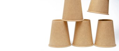 Kahve, çay için kahverengi kağıt bardak, beyaz arka planda çevresel malzemelerden bir içecek. Erkek el makro ve genel plan olarak bir fincan piramidi inşa eder. Metni sol ve sağ tarafa yerleştir.