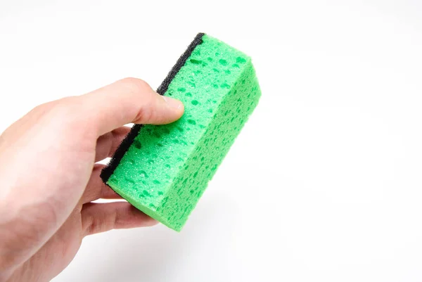 Sponge for washing dishes on a white background. Washcloth of green and yellow color. The male hand holds a sponge, green washcloth sideways and a top view, from the first person