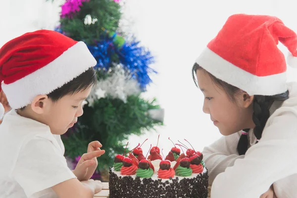 Glada asiatiska barn i jul hatt med julkaka — Stockfoto