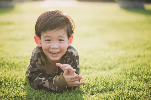Şirin Asyalı çocuk güneş ışığı altında greeen çim üzerinde yalan — Stok fotoğraf