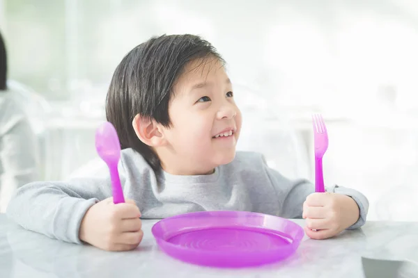 Asiatiska barn håller en sked och gaffel med Tom platta i restau — Stockfoto