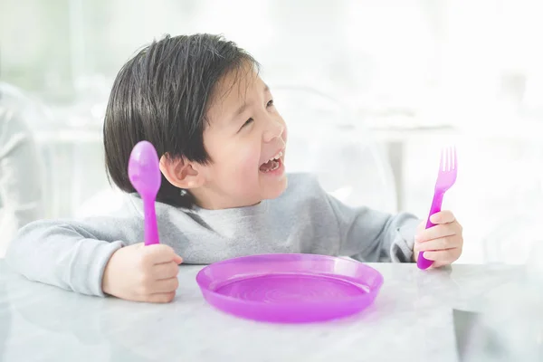 Asiatiska barn håller en sked och gaffel med Tom platta i restau — Stockfoto