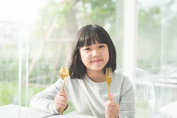 Beautiful Asian girl holding a spoon and fork with empty white plate in restaurant — Stock Photo, Image