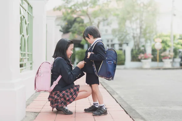 Азиатская школьница помогает одевать униформу своего брата — стоковое фото
