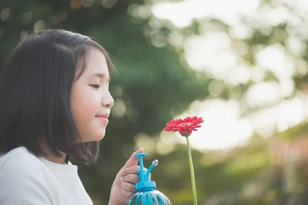 Menina asiática regando uma flor vermelha no jardim — Fotografia de Stock