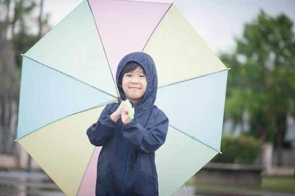 Fericit asiatic baiat holding colorat umbrelă joc în the parc — Fotografie, imagine de stoc