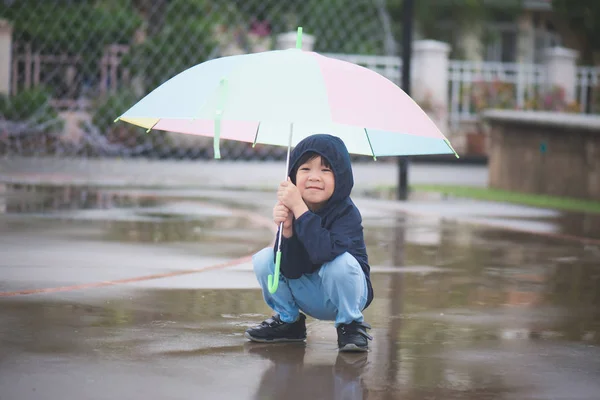 Glad asiatiska pojke innehar färgglada paraply spelar i parken — Stockfoto