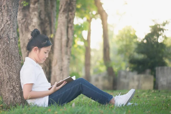 Ασιατικό κορίτσι διαβάζοντας ένα βιβλίο κάτω από το δέντρο — Φωτογραφία Αρχείου