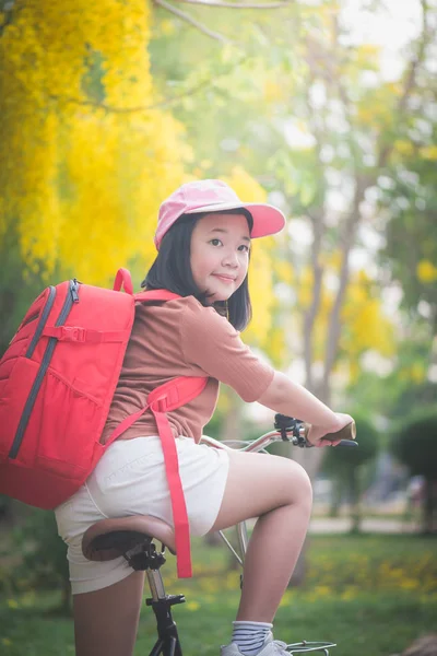 Hermosa chica asiática con mochila roja montar en bicicleta en el parque — Foto de Stock