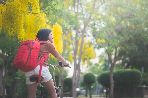 Красивая азиатка с красным рюкзаком на велосипеде в парке — стоковое фото