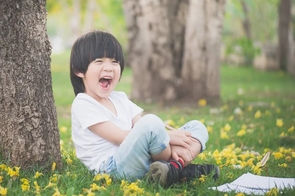 Kleine Aziatische jongen onder de boom zitten en tekening in notitieblok — Stockfoto