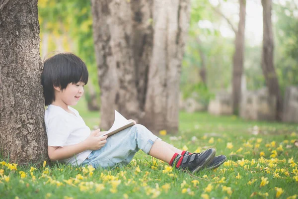 Liten asiatisk pojke sitter under trädet och ritning i anteckningsboken — Stockfoto