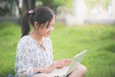 Dizüstü bilgisayar ile yeşil çimenlerin üzerinde parkta oturan güzel Asyalı kız