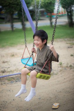 Parkta salıncak üzerinde oynarken kimono içinde şirin Asyalı çocuk
