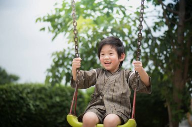 Parkta salıncak üzerinde oynarken kimono içinde şirin Asyalı çocuk