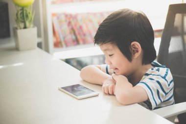 Mutlu Asyalı çocuk cep telefonuyla beyaz masaya