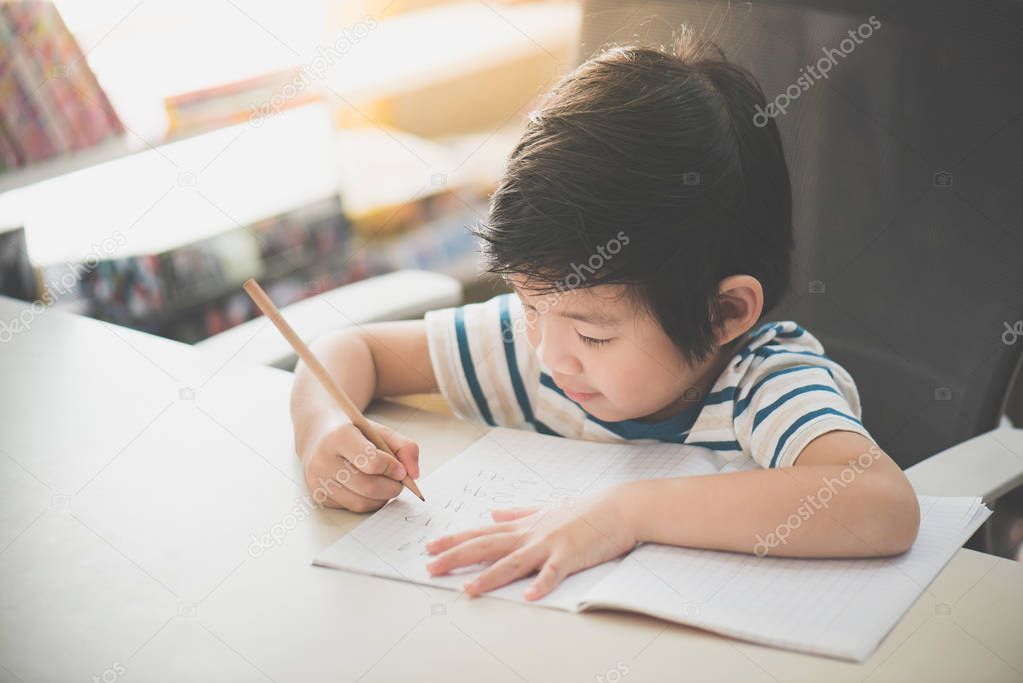 Little Asian child  using a pencil to write on notebook at the desk